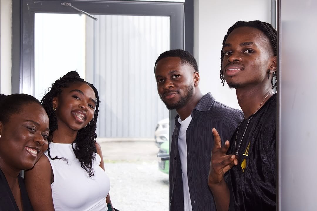 Four young adults smiling, standing near an open door