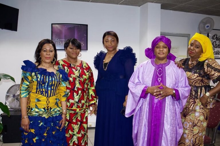 Five women dressed in colorful traditional African attire posing for a photo in a church setting
