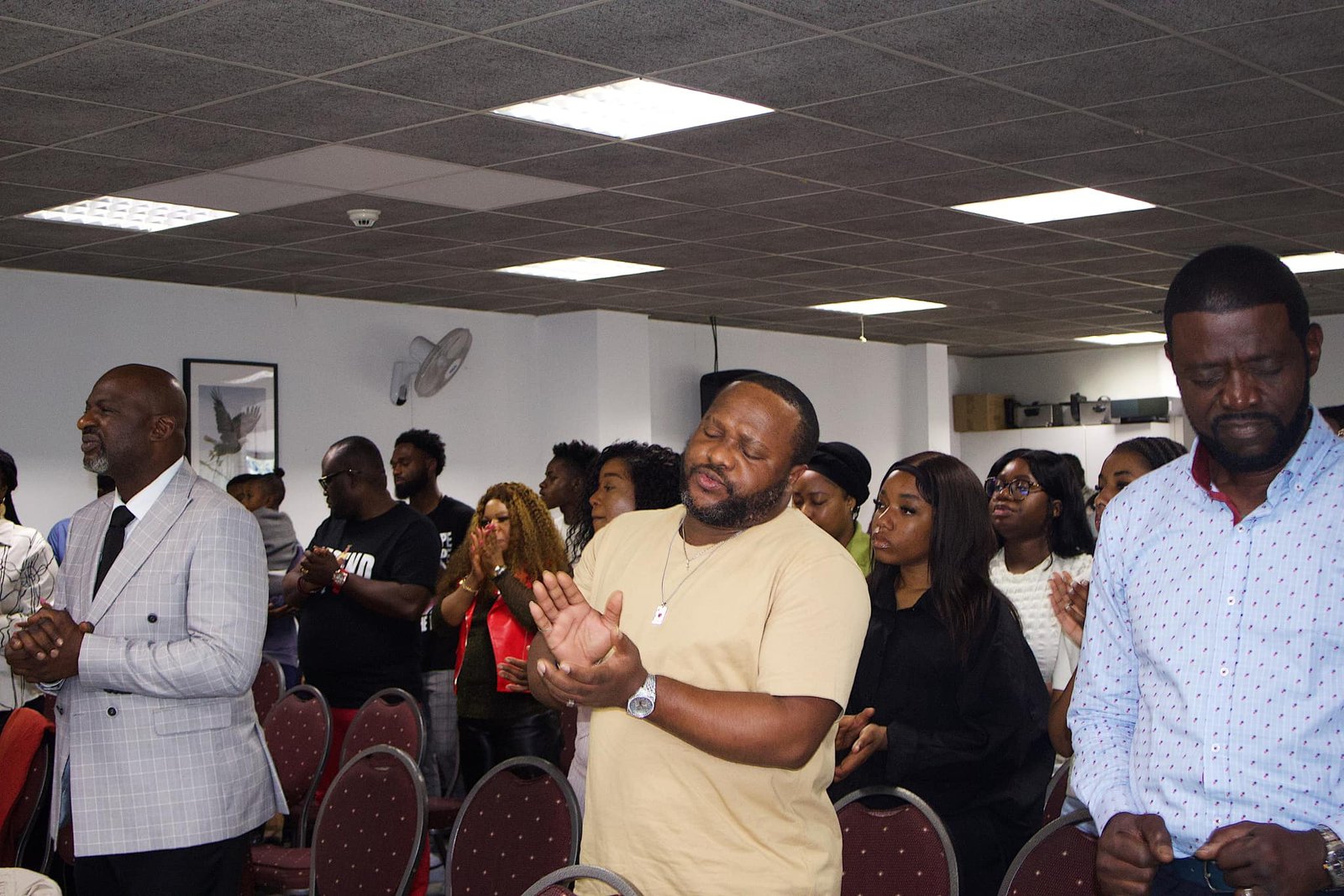 Group of church members participating in a testimony session, eyes closed and hands clasped in prayer.