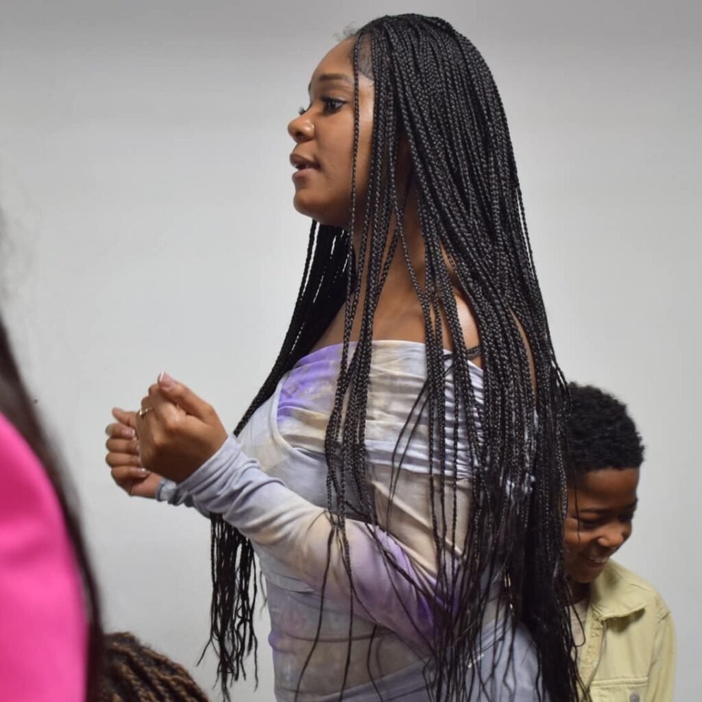 Young woman with long braided hair praying in church, surrounded by other congregants.