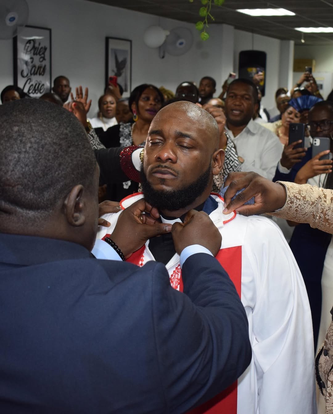 Pastor Dave Mukendi being adorned with a ceremonial scarf during a special service at Église La Bonne Semence, with congregation members witnessing the event.