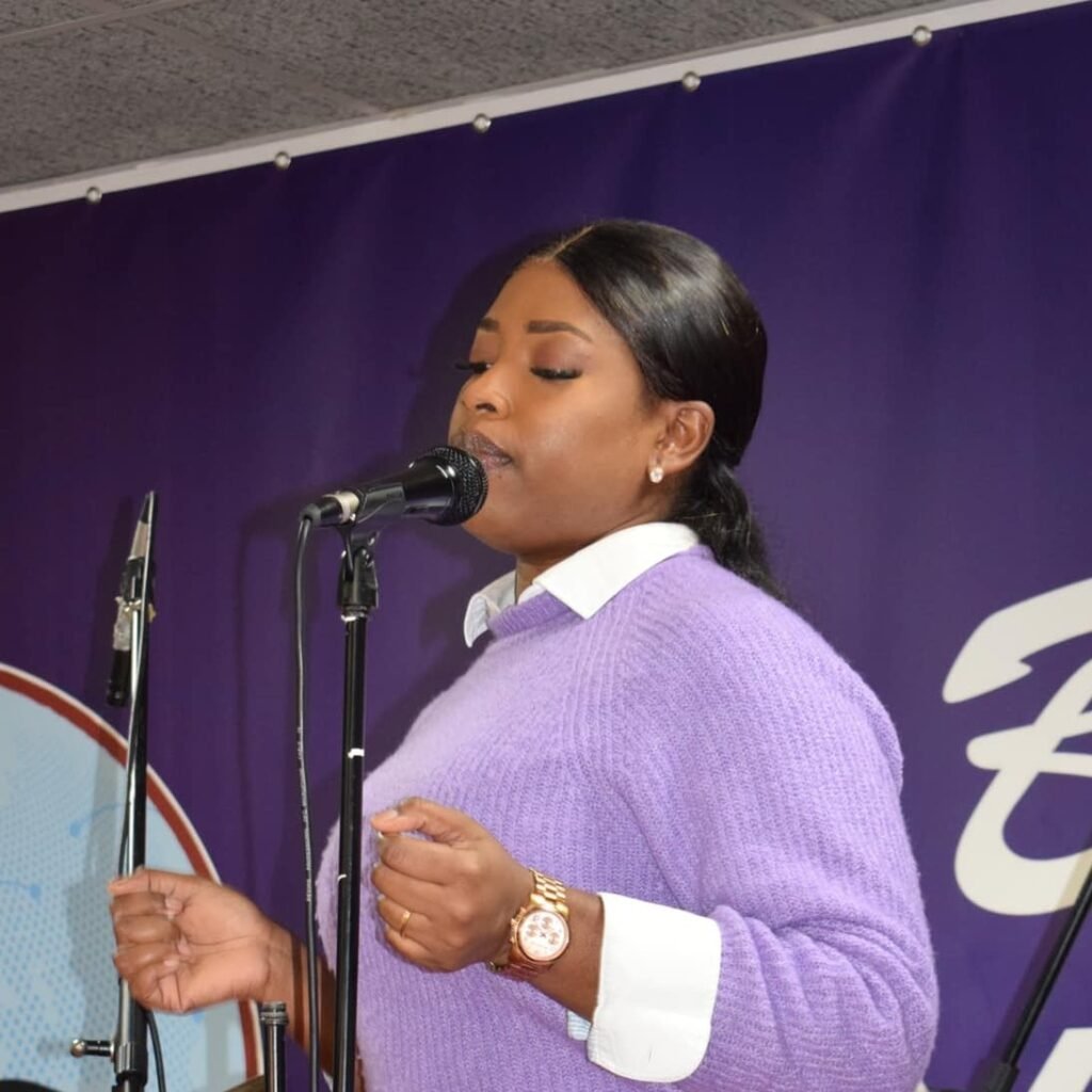 Tatiana singing into a microphone at a church event, clad in a purple sweater.