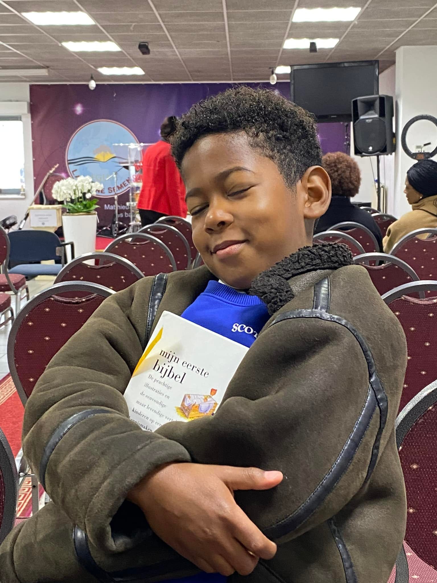 Young boy hugging his Bible with a content smile in a church setting