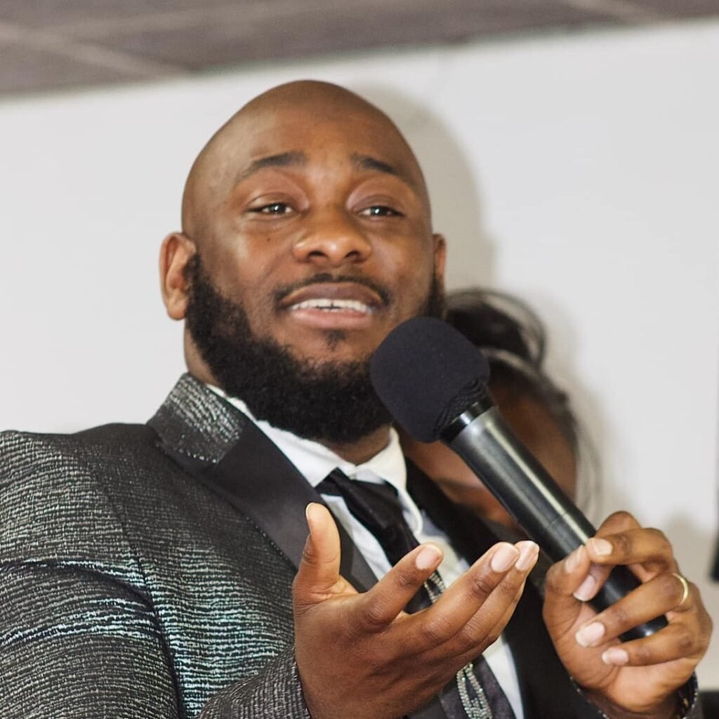 Close-up of Pastor David Mukendi speaking into a microphone, his hands expressively gesturing.
