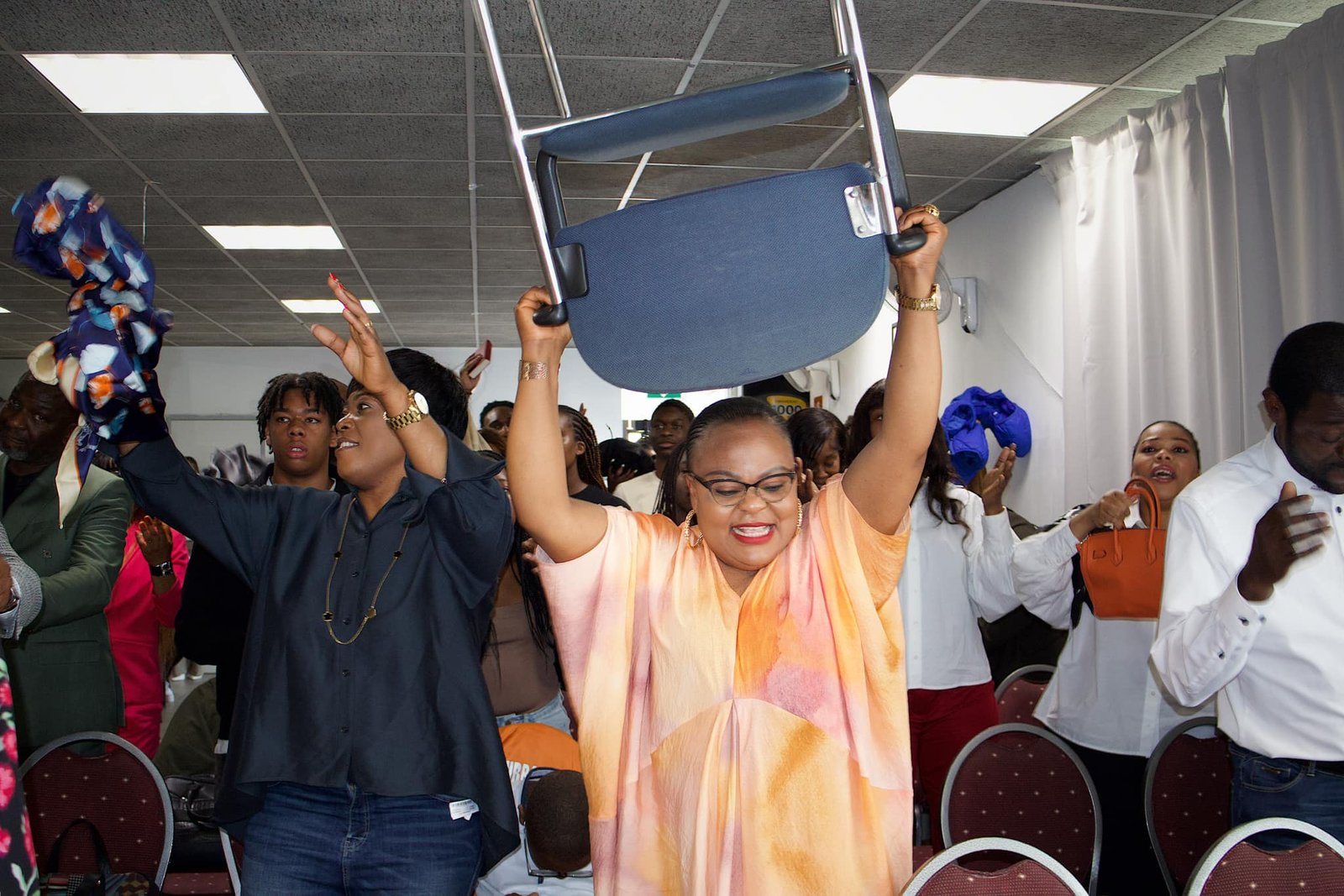 Congregation members at Église La Bonne Semence joyfully lifting chairs and waving items during a vibrant church celebration.