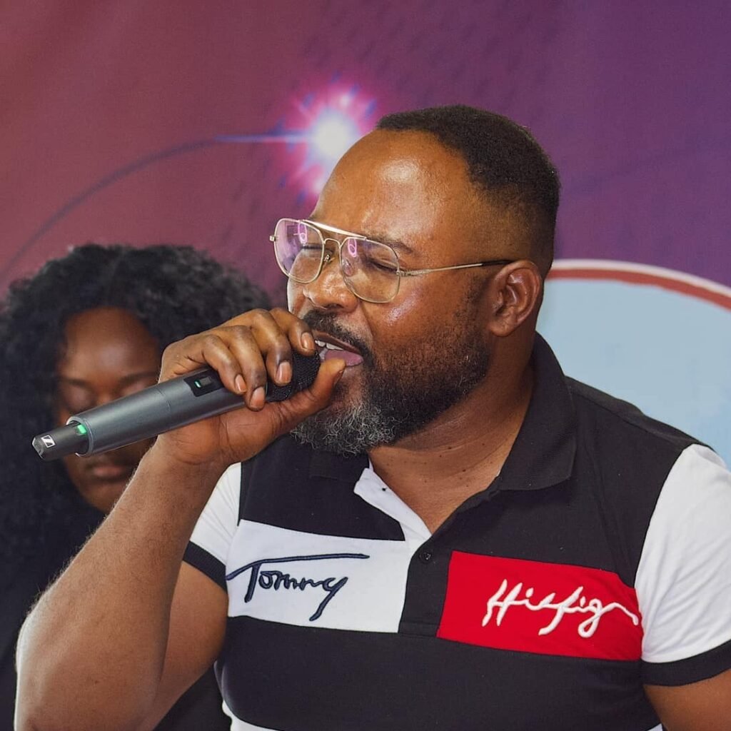 A man in a black and white Tommy Hilfiger polo shirt passionately singing into a microphone.