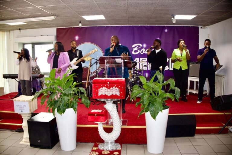 Church band performing on stage with vocalists and musicians, set against a purple-themed church backdrop.