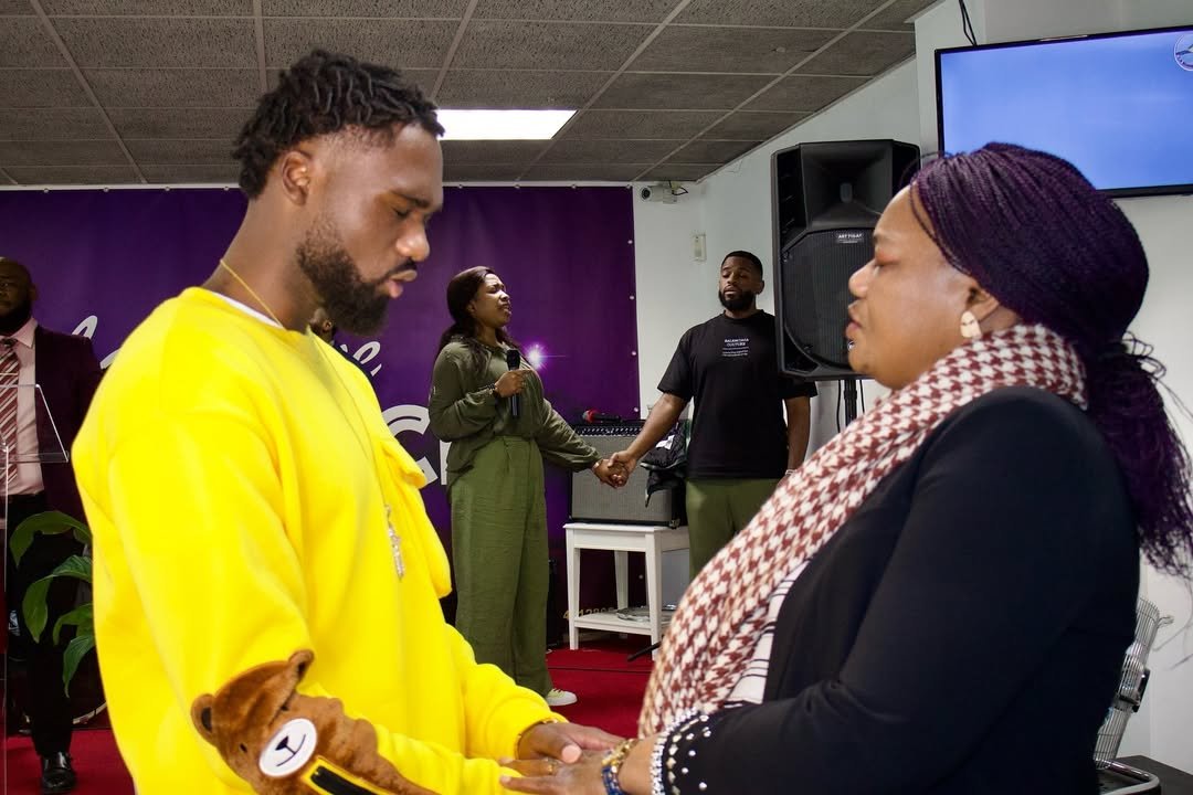 A man in a bright yellow sweatshirt and a woman in a black top and patterned scarf engaging in prayer at Église La Bonne Semence.