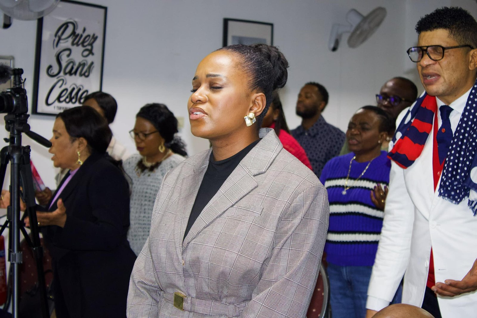 A woman in a plaid blazer with her eyes closed in a moment of contemplation, surrounded by other churchgoers.